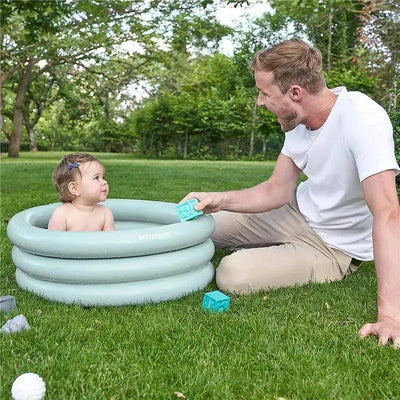Inflatable Babymoov baby bathtub in a grassy area with a smiling parent playing with a child inside.