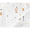 Muslin swaddle blanket featuring illustrations of Jesus, sheep, sun, and various symbols in soft colors.
