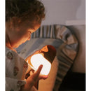Child smiling while holding a warm, glowing Jesus night light with a friendly design, in a cozy bedroom setting.