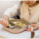 A toddler uses a pink Beaba 3Pk stainless steel cutlery set to eat pasta and veggies from a divided plate.
