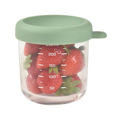 Beaba 8 oz glass baby food jar in sage, filled with fresh strawberries and marked with measurement indicators.