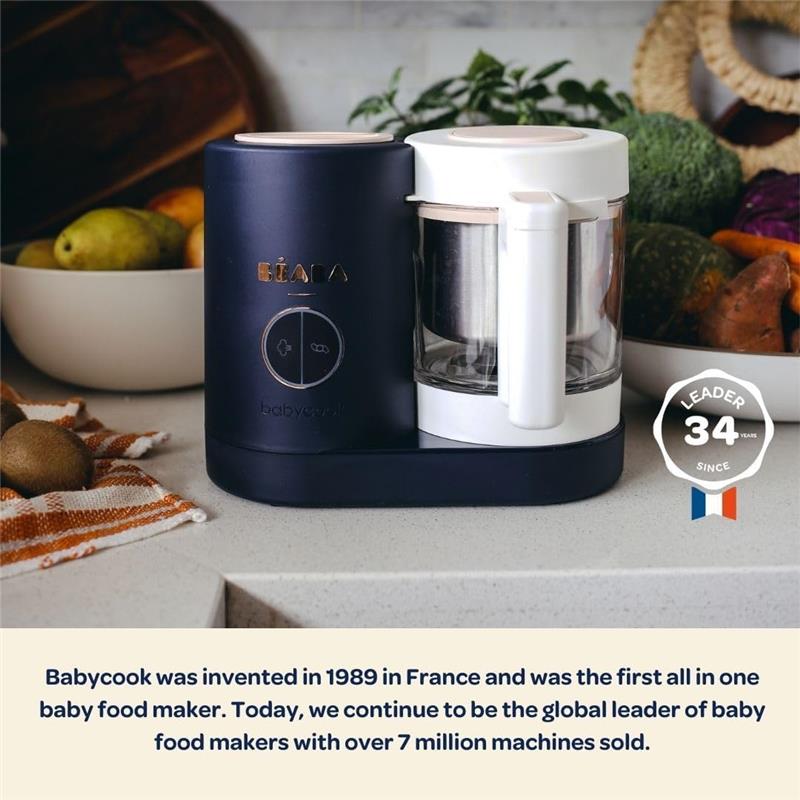Beaba Babycook Neo Baby Food Maker in cotton candy color, designed for steaming and blending baby food, with visible fruit in the background.