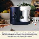 Beaba Babycook Neo Baby Food Maker in cotton candy color, designed for steaming and blending baby food, with visible fruit in the background.