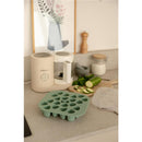 Béaba Silicone Mini Multiportion Tray in sage green on a kitchen counter with chopped cucumbers and a kitchen appliance.
