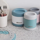 Beaba Stainless Steel Insulated Food Jar in Sage color, 10 oz, displayed among utensils and other jars on a countertop.