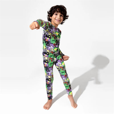 Boy in colorful Batman Baddies bamboo pajamas poses playfully, showing cartoon characters and vibrant patterns.