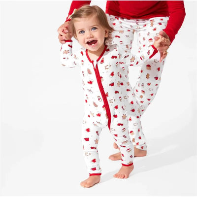 Toddler wearing a Christmas-themed bamboo footie with cookie prints, happily held by an adult in matching pajamas.
