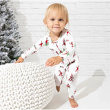 Toddler wearing Bellabu Bear Christmas pajamas featuring an Elf on the Shelf design, playing near a knitted pouf and a Christmas tree.
