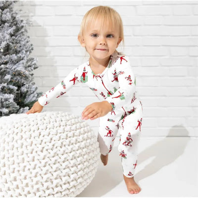 Toddler wearing Bellabu Bear Christmas pajamas featuring an Elf on the Shelf design, playing near a knitted pouf and a Christmas tree.