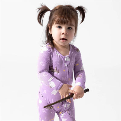 Toddler wearing a purple footie with Harry Potter designs, holding a wand, looking at the camera.
