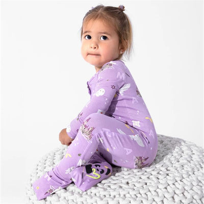 Toddler wearing a purple, Harry Potter-themed bamboo footie covered in owls and castle designs, sitting on a knitted blanket.