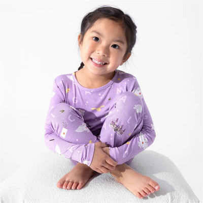Bamboo kids pajamas in purple featuring Harry Potter-themed graphics, worn by a smiling girl sitting cross-legged.