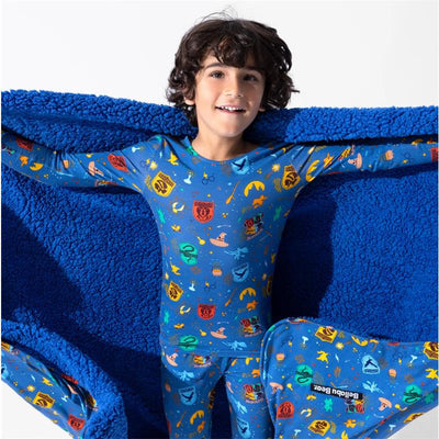 A smiling child wearing a Harry Potter-themed blue pajama set, holding a plush blue blanket featuring magical icons.