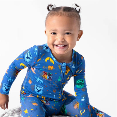Smiling toddler wearing a blue Harry Potter-themed bamboo footie, featuring colorful house crests and magical icons.