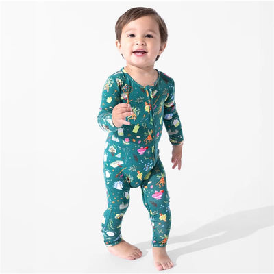 Toddler in a green bamboo footie covered with Harry Potter-themed mandrakes and herbs, smiling and standing.