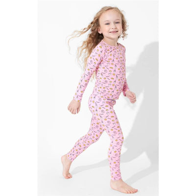 Pink bamboo pajamas for kids featuring a milk and cookies print, worn by a playful child aged 18-24 months.