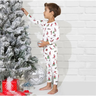 Boy in patterned bamboo pajamas reaching for an ornament on a frosted Christmas tree, with gifts nearby.