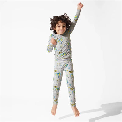 A young boy with curly hair is joyfully jumping while wearing grey toddler pajamas featuring Batman designs and colorful patterns.