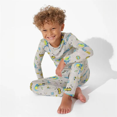Toddler boy with curly hair wearing Batman-themed bamboo pajamas, smiling while seated on the floor.