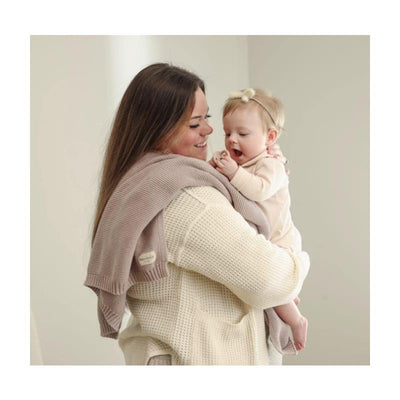 Luxury cotton swaddle receiving blanket draped on a woman holding a smiling baby, both in soft, neutral colors.