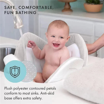 Plush grey baby bathtub cushion in a sink, featuring a smiling baby with a hand reaching towards the faucet.
