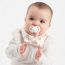 Baby with a pacifier wearing a pink rainbow-patterned bandana bib, clapping hands, smiling.