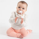 Baby wearing a pink bandana bib with rainbow print and holding a pacifier, sitting and clapping hands.