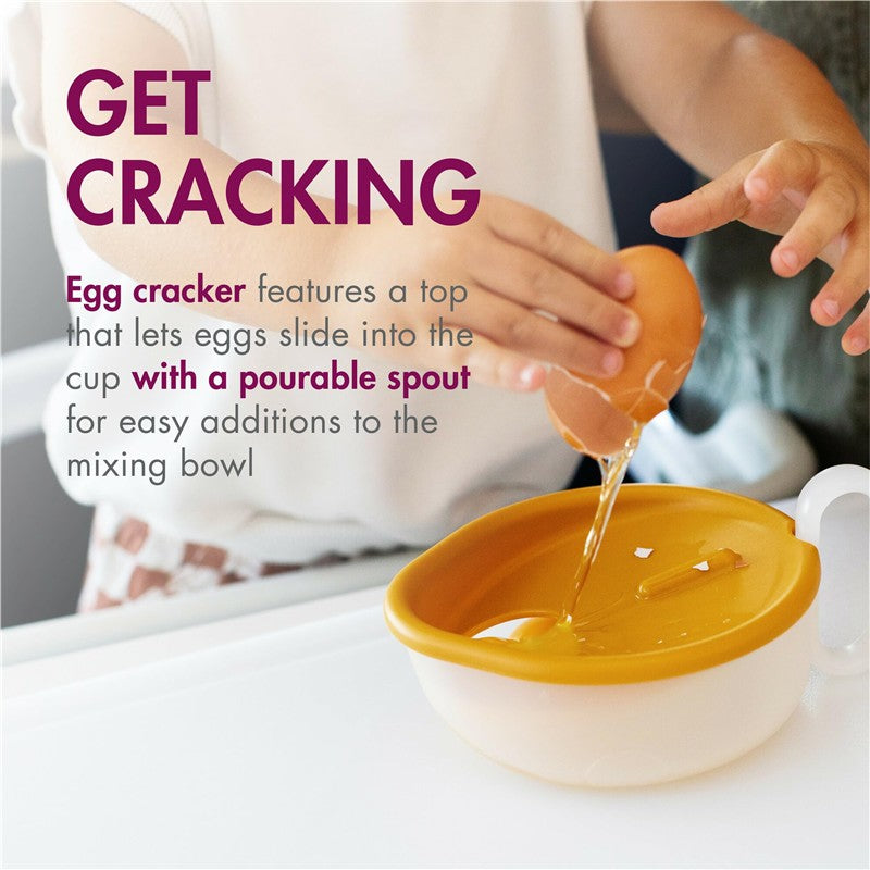 Toddler using the Boon INTRO egg cracker to crack an egg into a cup with a pourable spout for easy transfer.