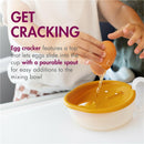 Toddler using the Boon INTRO egg cracker to crack an egg into a cup with a pourable spout for easy transfer.