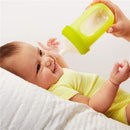 Boon NURSH silicone bottle with a yellow nipple held above a smiling baby in a striped onesie, feeding time.