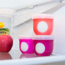 Boon NURSH Storage Caps 3-Pack displayed in a refrigerator, featuring colorful silicone lids in pink and red with white circles.