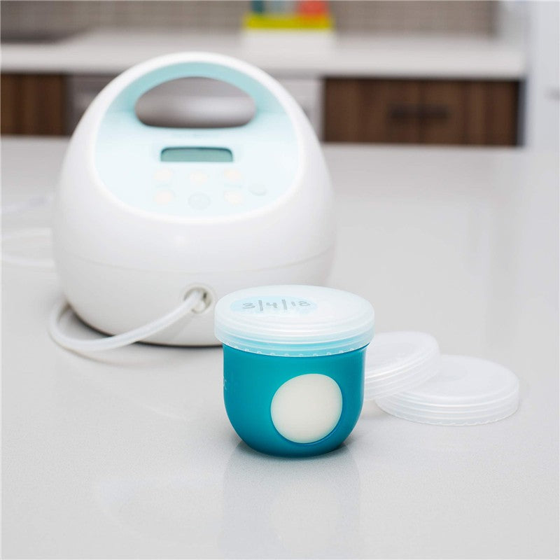 Boon NURSH Storage Caps 3-Pack featuring a teal storage container with a clear lid, positioned next to a milk pump on a countertop.