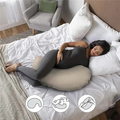 Pregnant woman relaxing on a bed, using a Boppy Cuddle Pregnancy Pillow with a beige organic cotton cover for support.