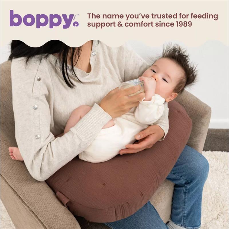 Boppy Nursing Pillow in Chestnut Muslin supports a mother feeding her baby with a bottle while seated.