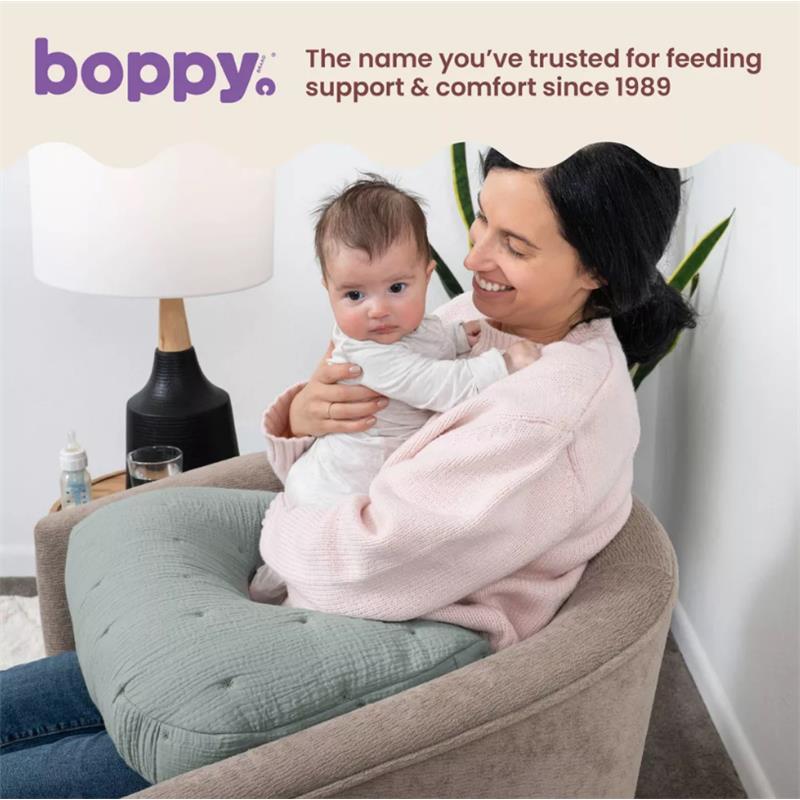 Mom comfortably holds a baby while using a Boppy Nursing Pillow in Chestnut Muslin, featuring a textured gray cover.