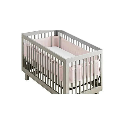 BreathableBaby Deluxe Ruffle Collection crib liner in blush color, securing to a wooden crib with a white mattress.