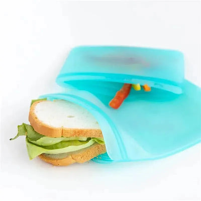 Silicone flat reusable bag in blue, containing a sandwich with lettuce and colorful carrot sticks peeking out.