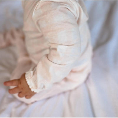 Light pink bodysuit with ruffled cuffs worn by an infant, emphasizing softness and comfort.