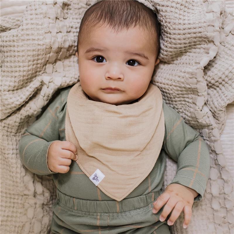 Baby wearing a tan bandana bib, nestled in a soft, textured blanket, with a neutral green outfit and gentle expression.
