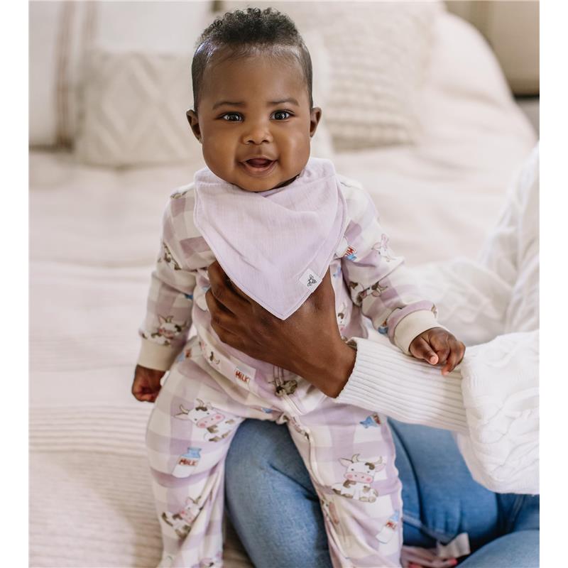 Baby smiles while wearing a pale purple bandana bib and a patterned pajama, held by an adult.