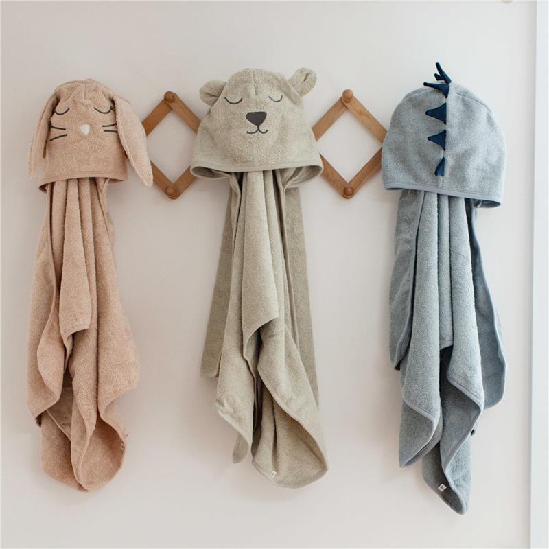 Hooded towels for toddlers displayed on a wall, featuring a bunny, bear, and dinosaur design in soft colors.