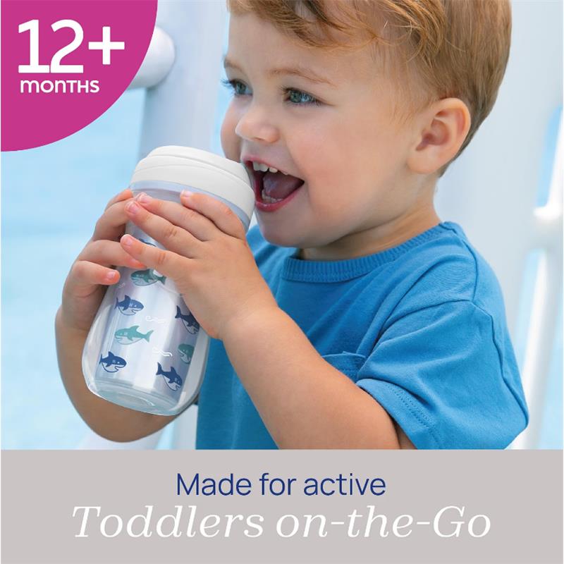 Chicco Insulated Rim Spout Trainer Sippy Cup in blue with shark designs, held by a toddler smiling while drinking.