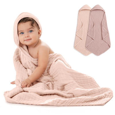 Hooded baby towels in mauve and blush draped around a smiling baby sitting on a soft surface.