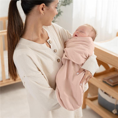 Mother holding a sleeping baby swaddled in a light blush blanket, showcasing the Comfy Cubs swaddle with zipper closure.