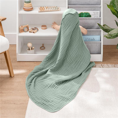 Hooded baby towel in fern green draped over a child, surrounded by toys on shelves and a plant.