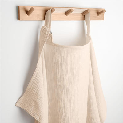Muslin nursing cover in sand color hanging on a wooden rack, showcasing its lightweight and breathable texture.