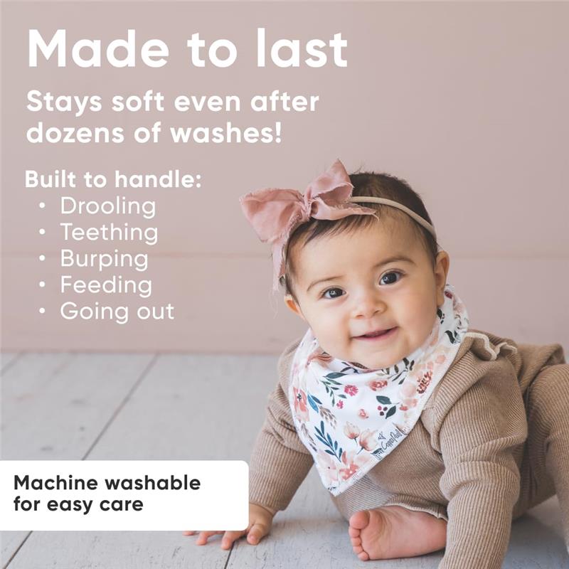 Baby wearing a floral Copper Pearl bandana bib, sitting on a floor with a soft smile, showcasing product features.