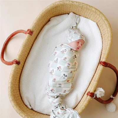 Baby swaddled in a Mickey Mouse & Friends knit blanket, peacefully sleeping in a woven bassinet.