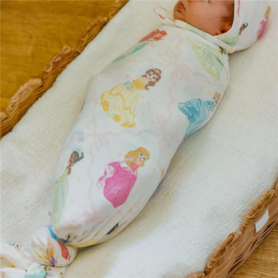 Blanket featuring Disney Princess designs, swaddling a sleeping baby in a wicker basket.