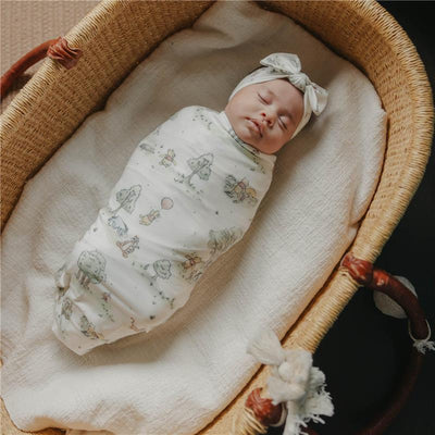 Large premium knit baby swaddle blanket featuring Hundred Acre Wood characters, wrapped around a sleeping infant in a bassinet.